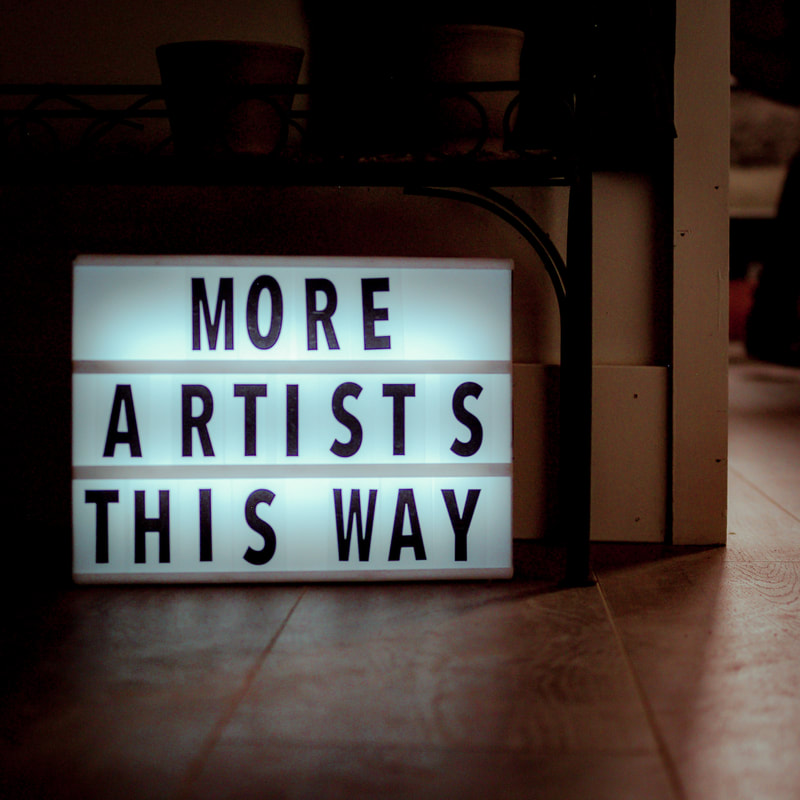 A dark room with a mini cinematic sign lit up saying 'More artists this way'. 