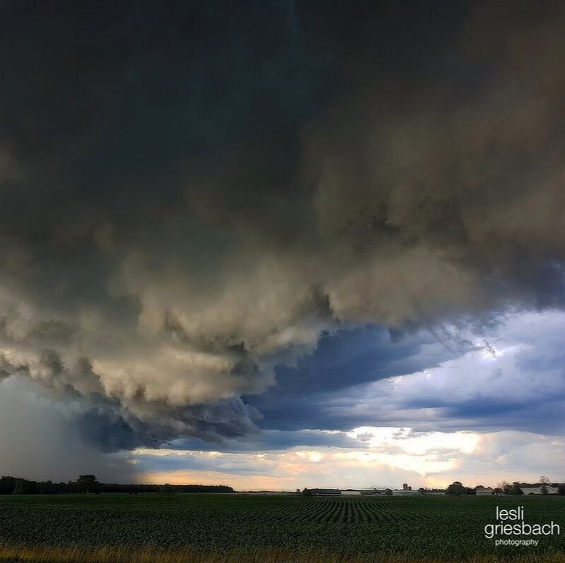 this is an image of a farmer's field. There is a storm front coming in on the left, so the sky is a mixtures of blue and grey clouds with the sun setting in the bottom right corner. The bottom third of the photo is of a green field
