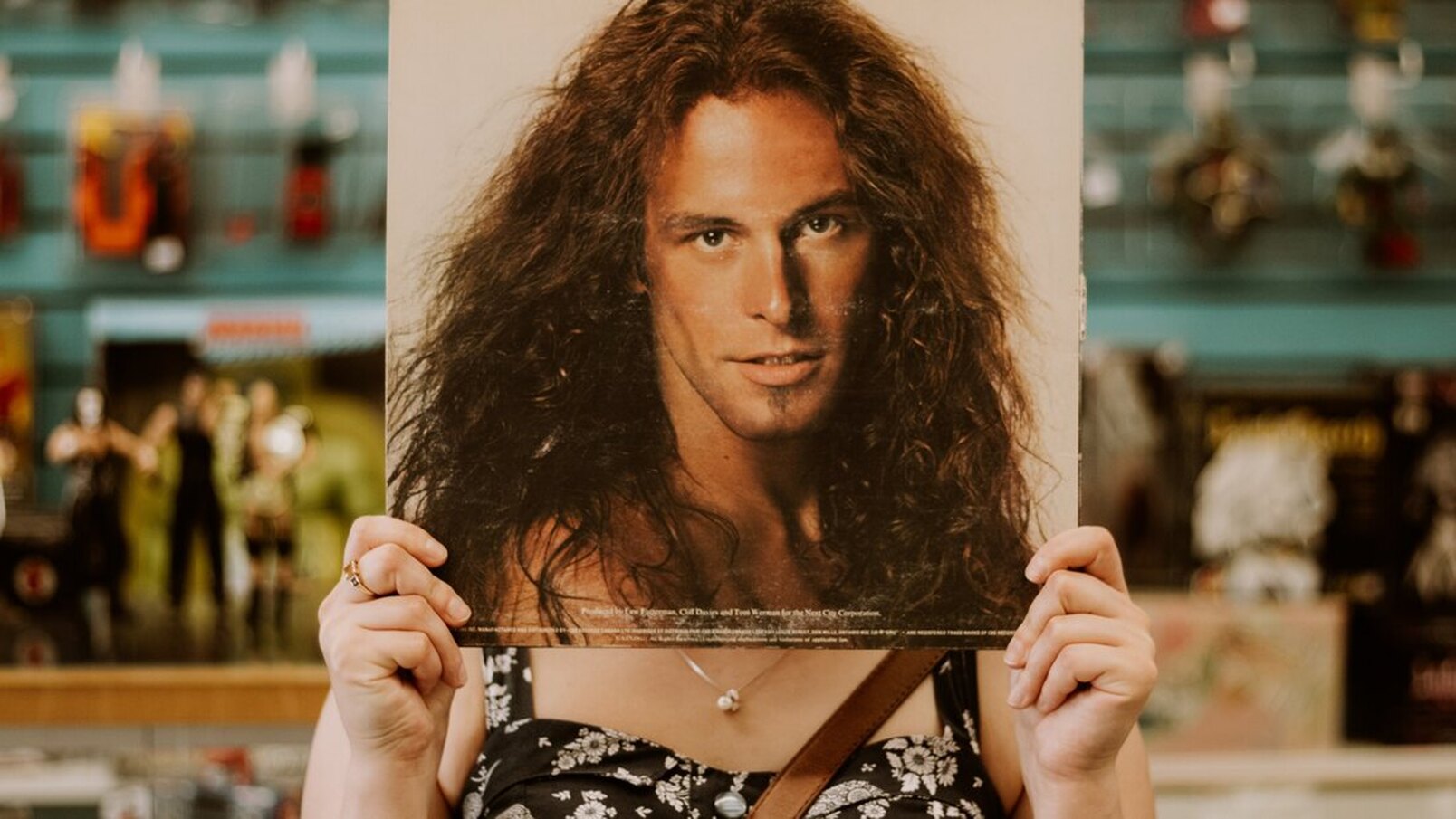 Here is an image of a woman holding up a record cover over her face. The cover is of a man with long curly hair.
