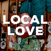 The background is of the Anything Is Possible boxcar mural. It shows a woman with blue hair, a green polka dot shirt, red scarf and pink skin. She is blowing bubbles. Above this photo is the text 'Love Local' in big, thick, white lettering.