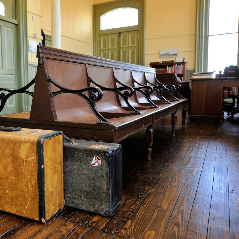 Here are some bench seats in the Military Museum . On the end of the bench are two suitcases. A tan suitcase with a black outline is in front and then there is a black suitcase behind it. 