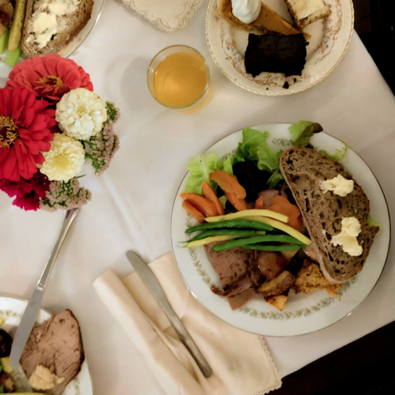 To the right of the image is a meal by Quaker House. There is lettuce, green beans, carrots, potatoes, meat and bread. There is a vase of colourful flowers in the top left corner. 